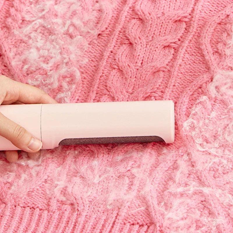 Hand using lint remover brush to clean pet hair from pink knit sweater