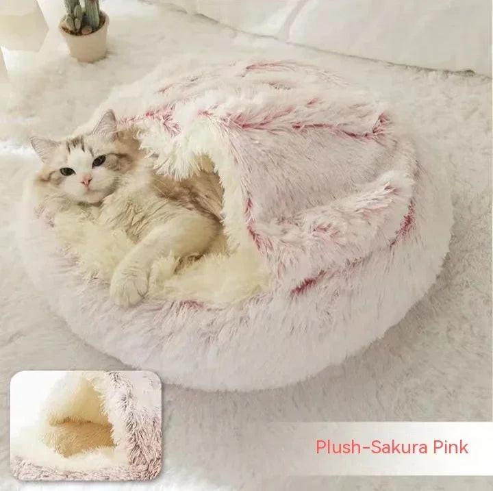 Cat relaxing in a round plush sakura pink pet bed with cozy cave design on a white blanket.