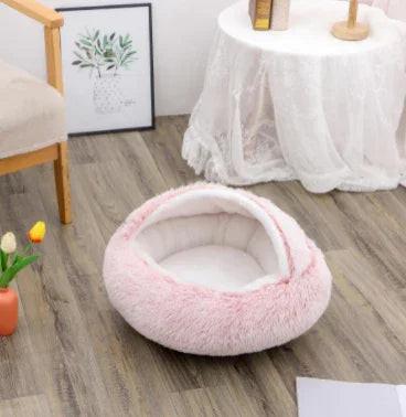 Plush pink pet bed with hood on wooden floor, cozy indoor dog and cat accessory