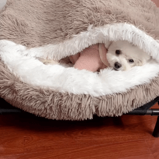 Small dog snuggled in a cozy, fluffy pet cave bed on a wooden floor