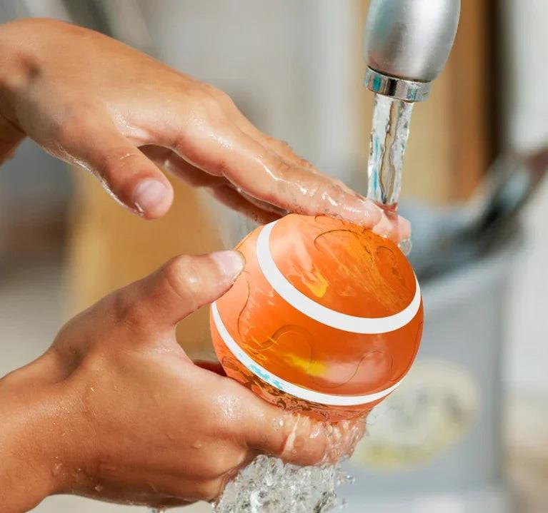 Person washing an orange pet toy ball under running water at a sink